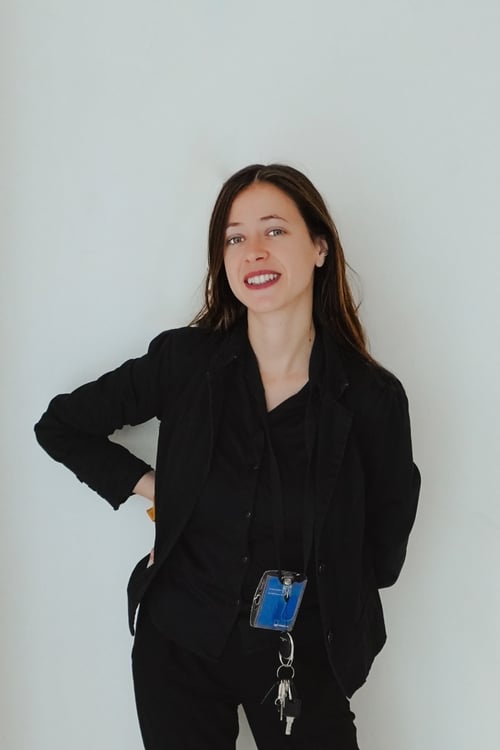 Professional portrait of Pauline, a smiling woman in a black blazer with an ID badge and keys, against a white background.