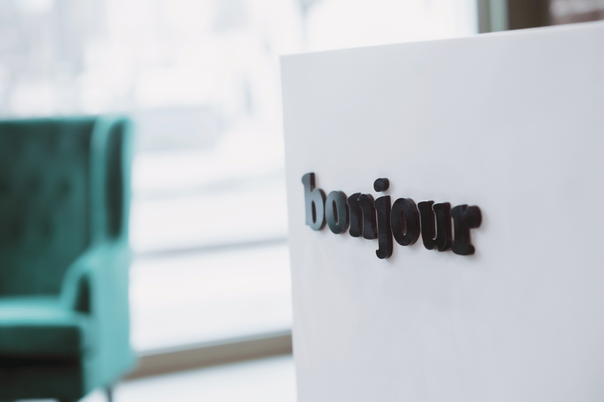 Black "bonjour" letters on a white sign with a blurred teal armchair in the easyHotel Paris Nord Aubervilliers lobby.