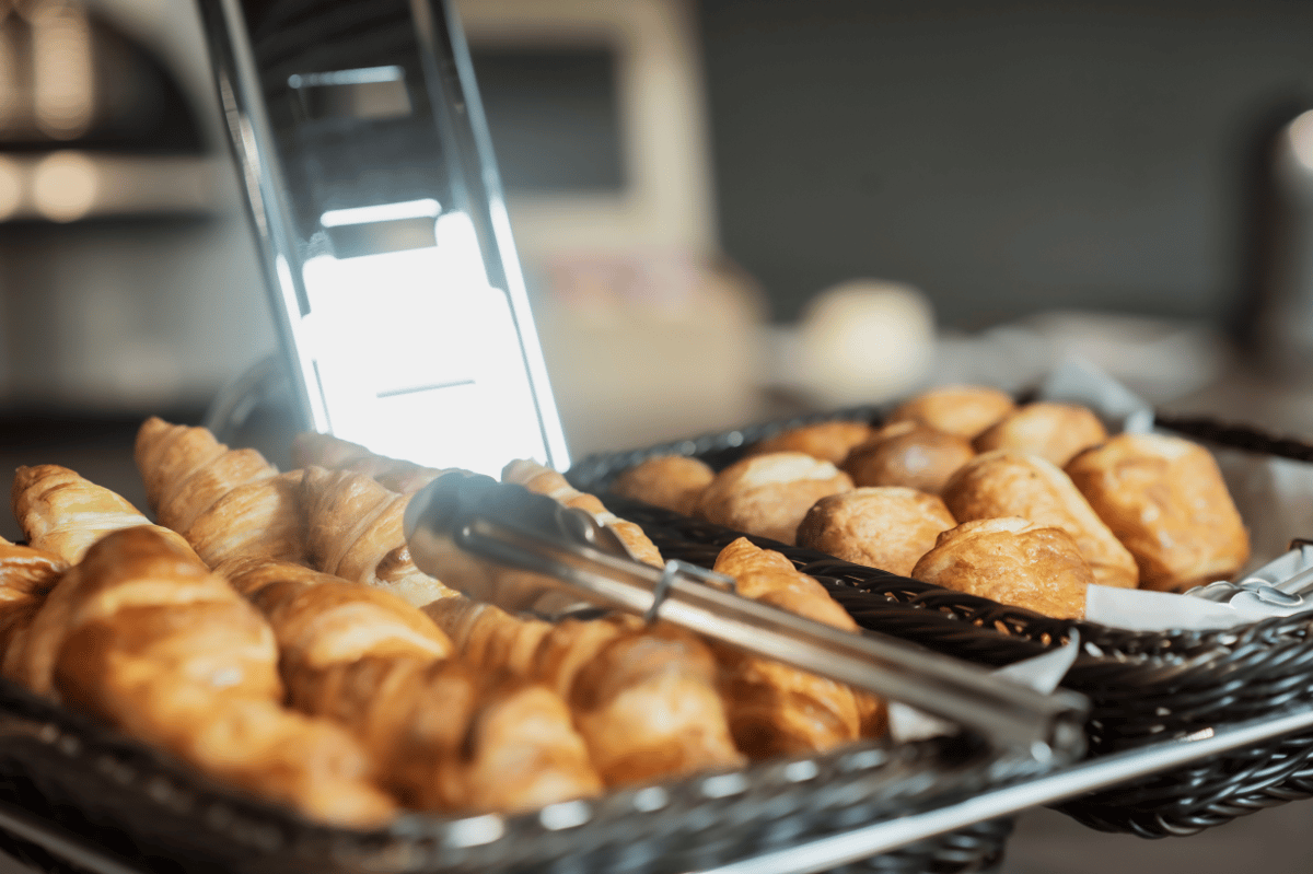 Golden croissants and pastries in woven baskets with serving tongs, presented at the easyHotel Paris Nord Aubervilliers breakfast buffet.