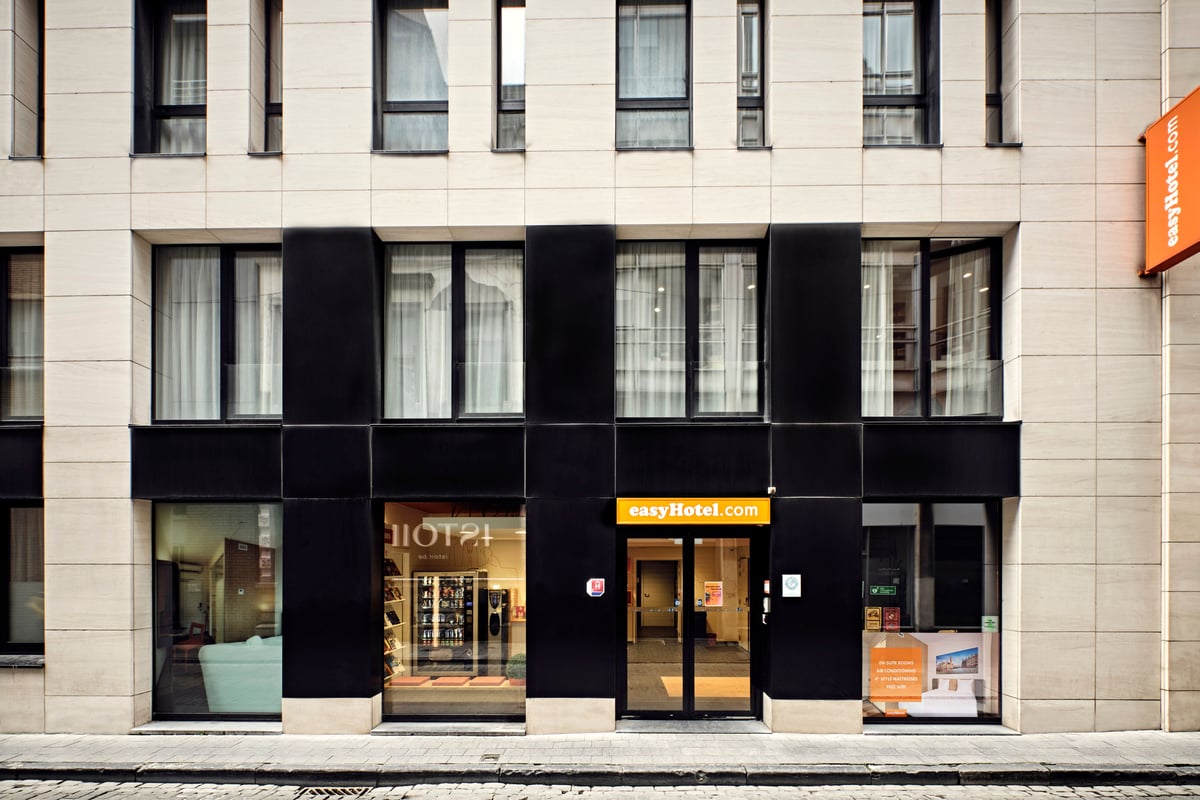 Exterior of the easyHotel Brussels City Centre, showcasing its modern facade with light-colored stone and dark black sections, large windows, and a prominent orange easyHotel.com sign above the entrance.