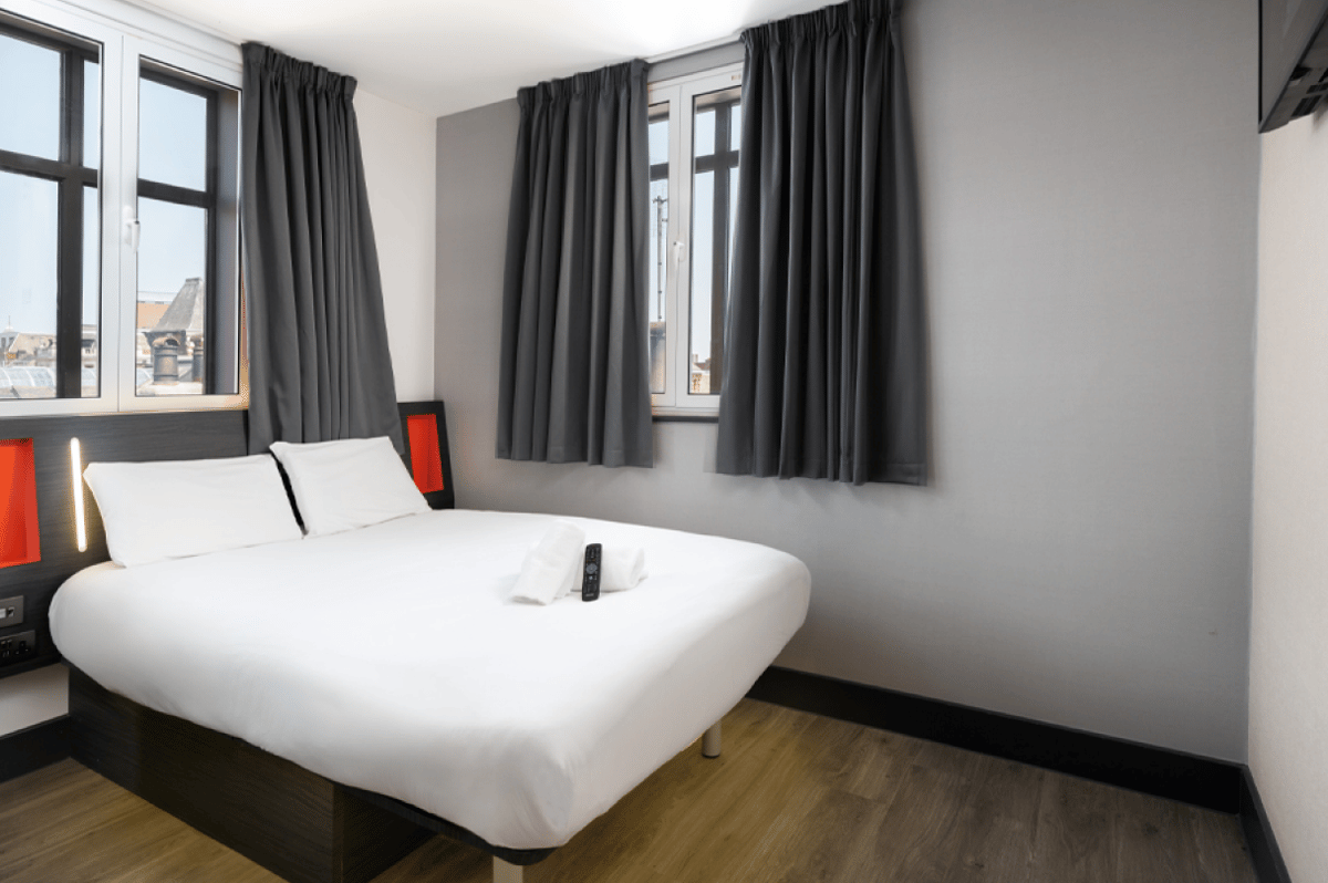 easyHotel Leeds room with a clean double bed, white bedding, dark grey curtains, and minimalist decor.