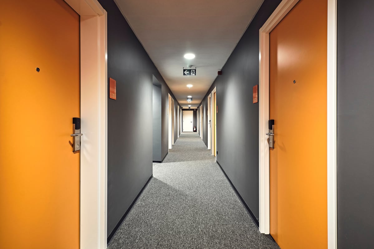 A long, modern easyHotel corridor in Brussels City Centre with dark grey walls, grey carpet, and bright orange guest room doors.