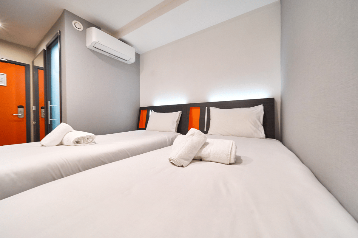 easyHotel London City Shoreditch twin room with two single beds, white linens, air conditioning, and a distinctive orange door.