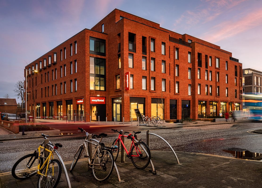 ALT text: EasyHotel London Old Street building exterior at dusk, showcasing modern red brick architecture with multiple large windows, prominent easyHotel signage, and a blurred double-decker bus on the street.