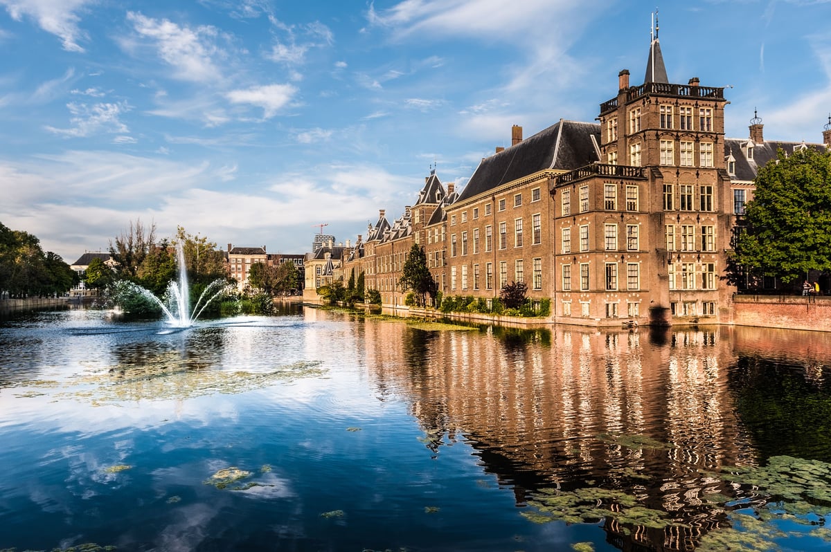 Historic Binnenhof government buildings reflecting in the Hofvijver pond with a fountain in The Hague, Netherlands.