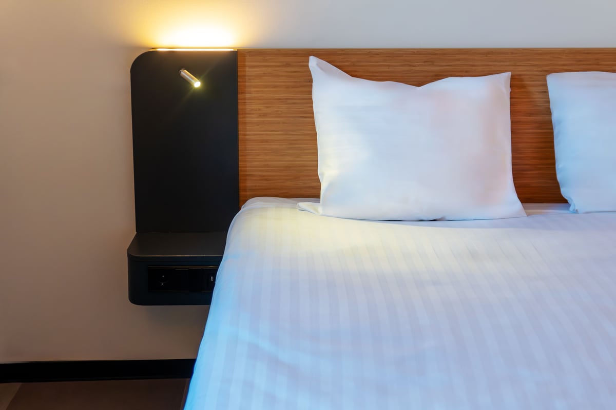 EasyHotel Amsterdam Arena Superior Double hotel room bed, featuring crisp white linen, a wooden headboard, and a modern bedside lamp.