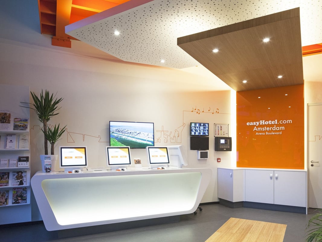 easyHotel Amsterdam Arena Boulevard reception area with modern white self-service check-in kiosks and a bright orange branded wall.