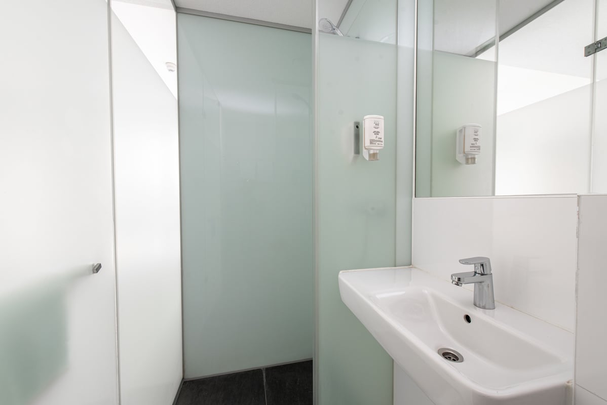 Compact, modern easyHotel Amsterdam bathroom featuring a white wall-mounted sink with chrome faucet and a frosted glass walk-in shower with a mounted soap dispenser.