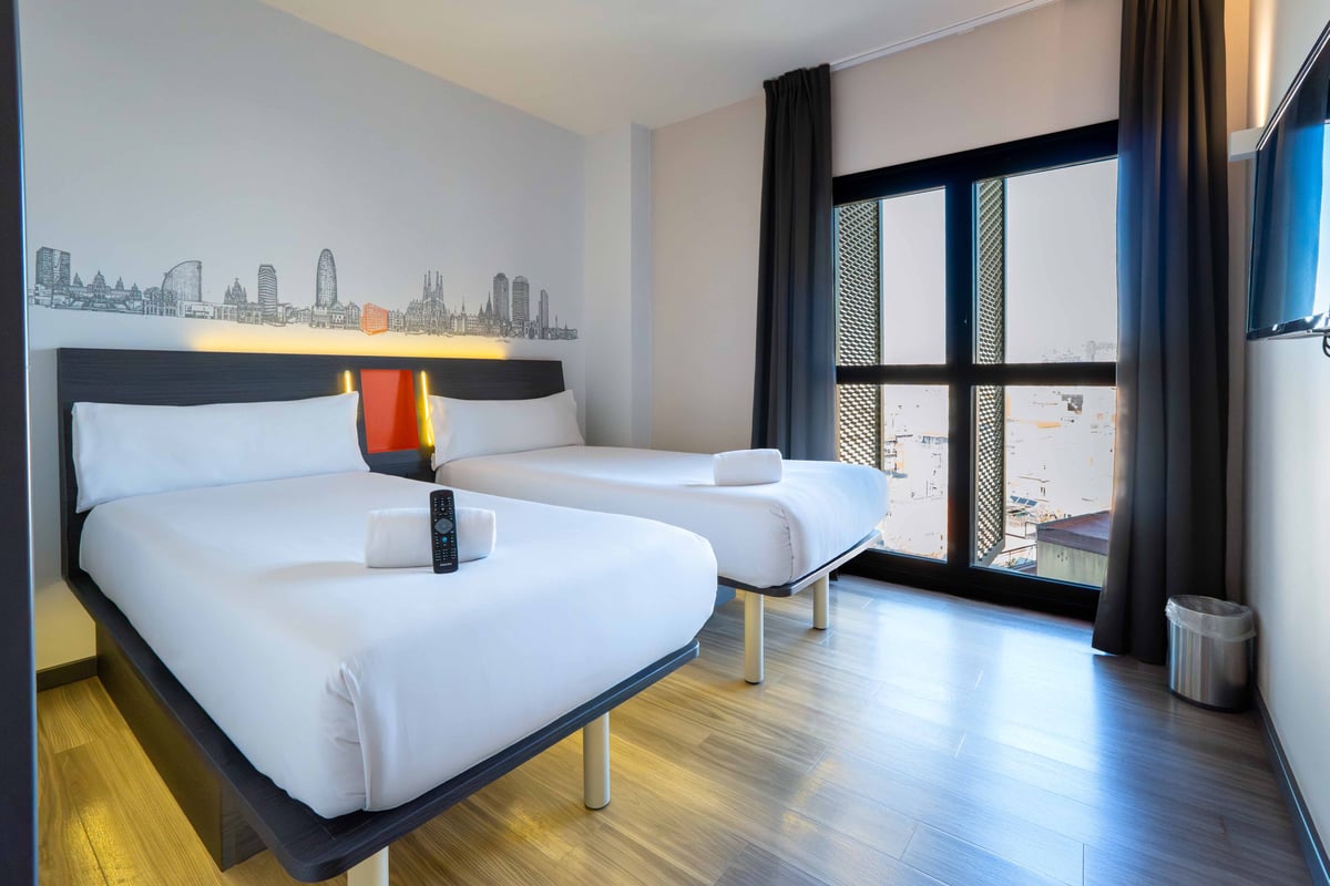 EasyHotel Barcelona Fira twin room with two single beds, white linens, and a city skyline graphic on the wall.