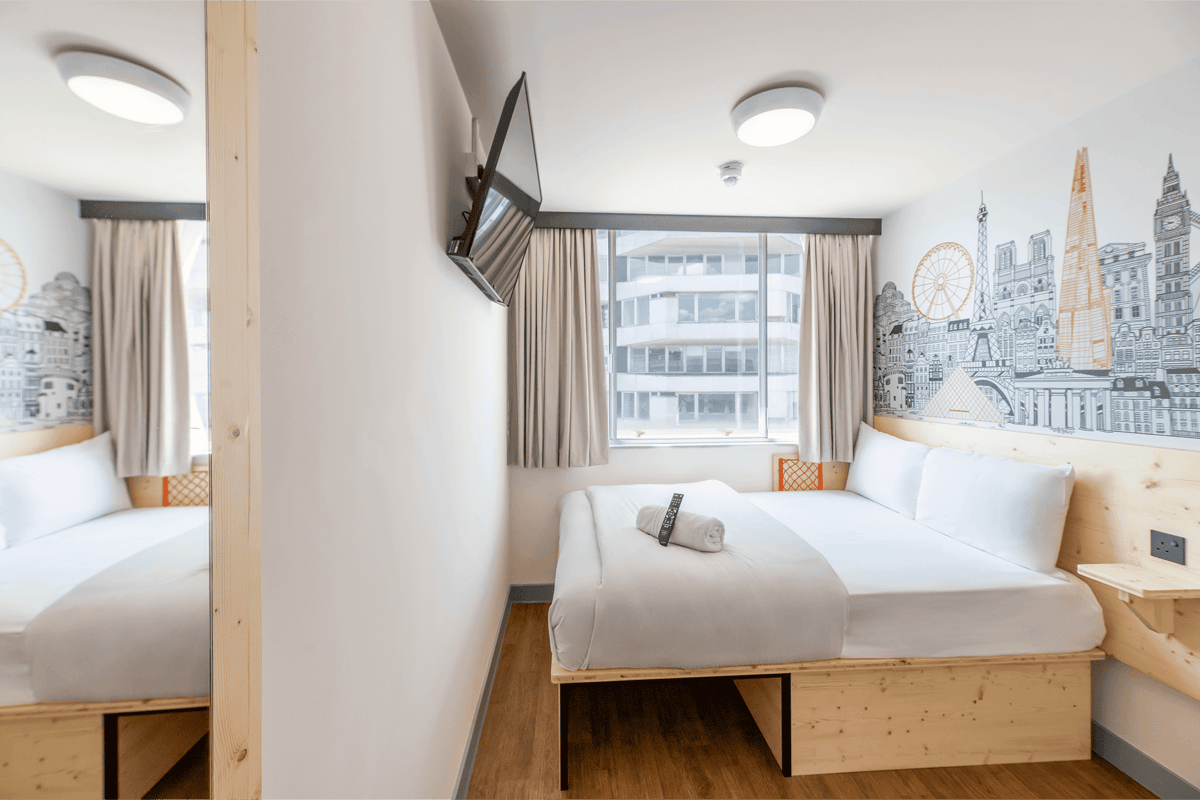 EasyHotel Croydon double room with double bed, white linens, and city-themed wallpaper.