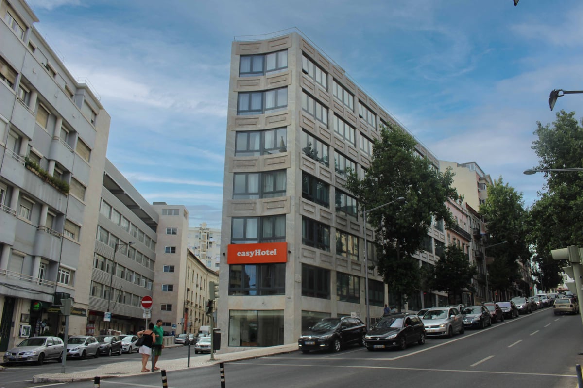 easyHotel Lisbon, Portugal at dusk, showcasing its distinctive facade illuminated with vibrant, multi-colored rectangular lights on a city street with traffic and streetlights.