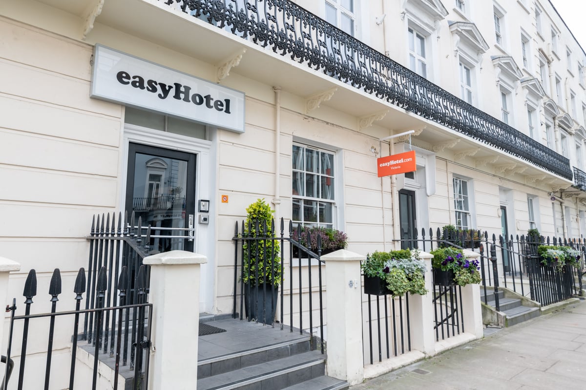 easyHotel London Victoria exterior, featuring a cream-colored facade, black wrought iron railings, steps leading to the main entrance, and window boxes with green plants.