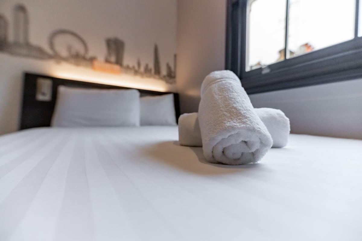 Clean easyHotel London Victoria family quadruple room with white linen, rolled towels, and a London skyline wall mural.
