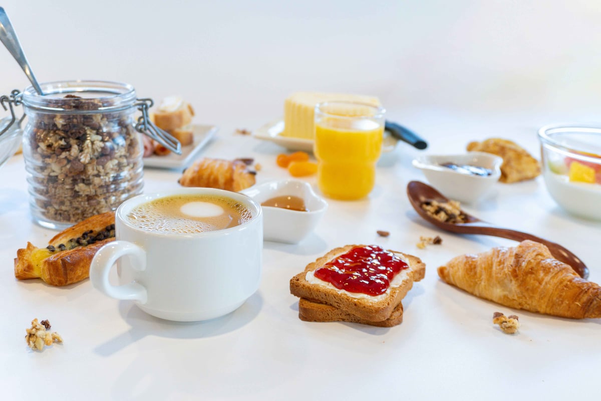 EasyHotel breakfast spread with coffee, croissants, toast with jam, cereal, juice, and butter on a white table.