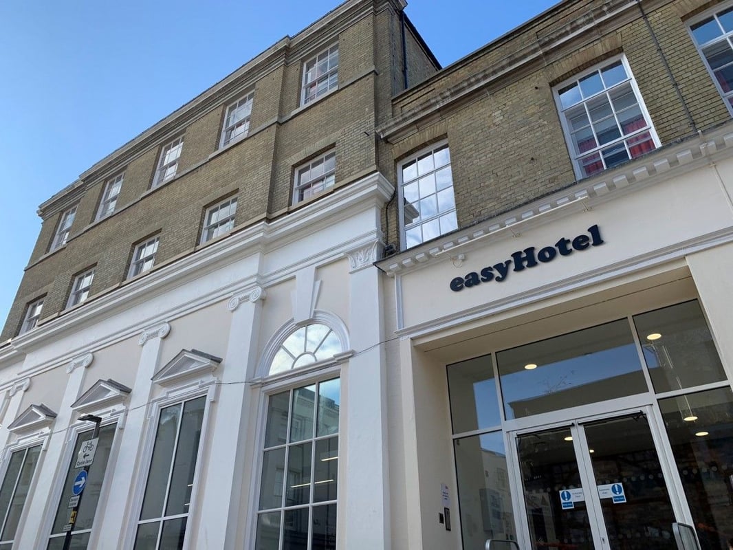 Exterior view of easyHotel Ipswich building, featuring its modern entrance with large glass windows on the ground floor and light brick upper levels, set against a clear blue sky.