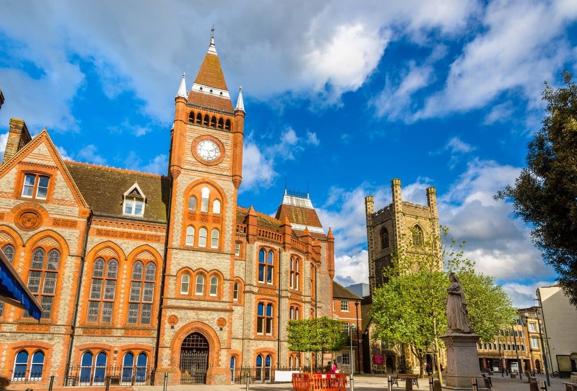 Historic Reading Town Hall and clock tower, alongside St Laurence Church and Queen Victoria statue, under a bright blue sky in Reading, UK.