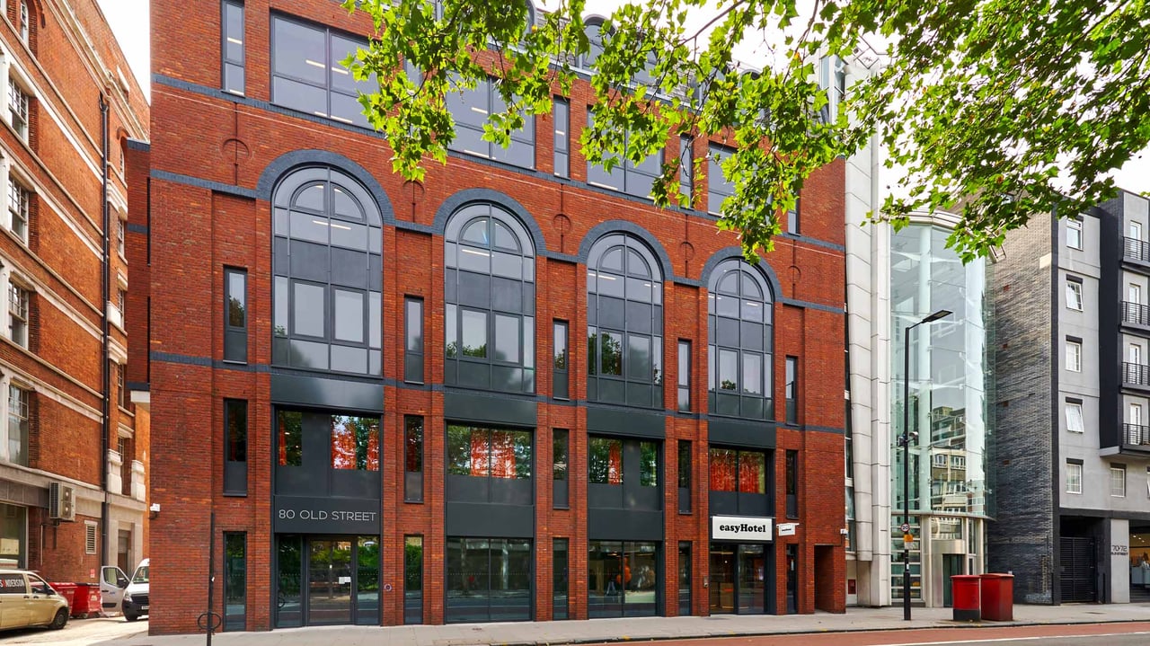Exterior view of the easyHotel on 80 Old Street, London. The modern red brick building features large arched windows and a prominent easyHotel sign at street level.